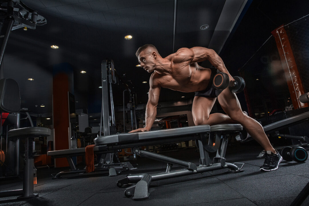 Bodybuilder performing a dumbbell row in a dimly lit gym to show Serious Supplements For Serious Performance